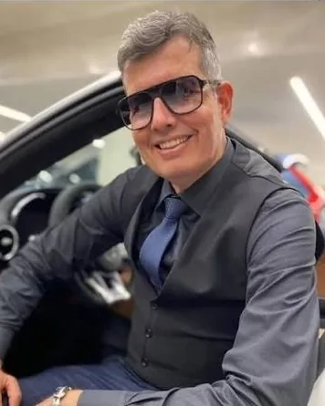 Conselheiro Fantasma, de óculos escuros e colete, sorrindo sentado num carro esportivo