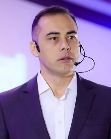 Thiago Magalhães, de terno, falando com microfone de cabeça
